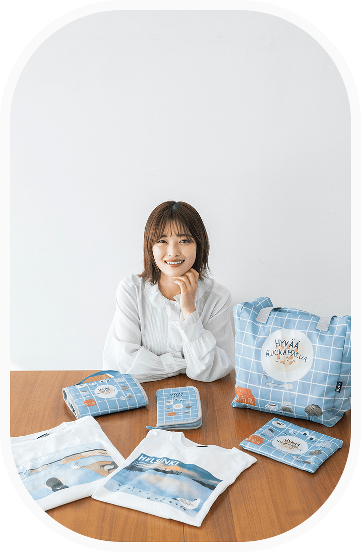 【メインイメージ】座っている井上咲楽さんの前に、コラボアイテムが机の上に並んでいます