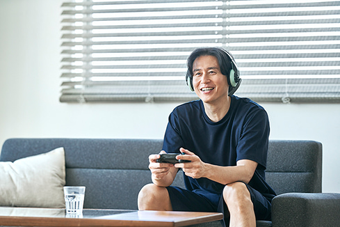 ソファでゲームをしながらRecoverypro Lab.の疲労回復ウェアを着用する男性
